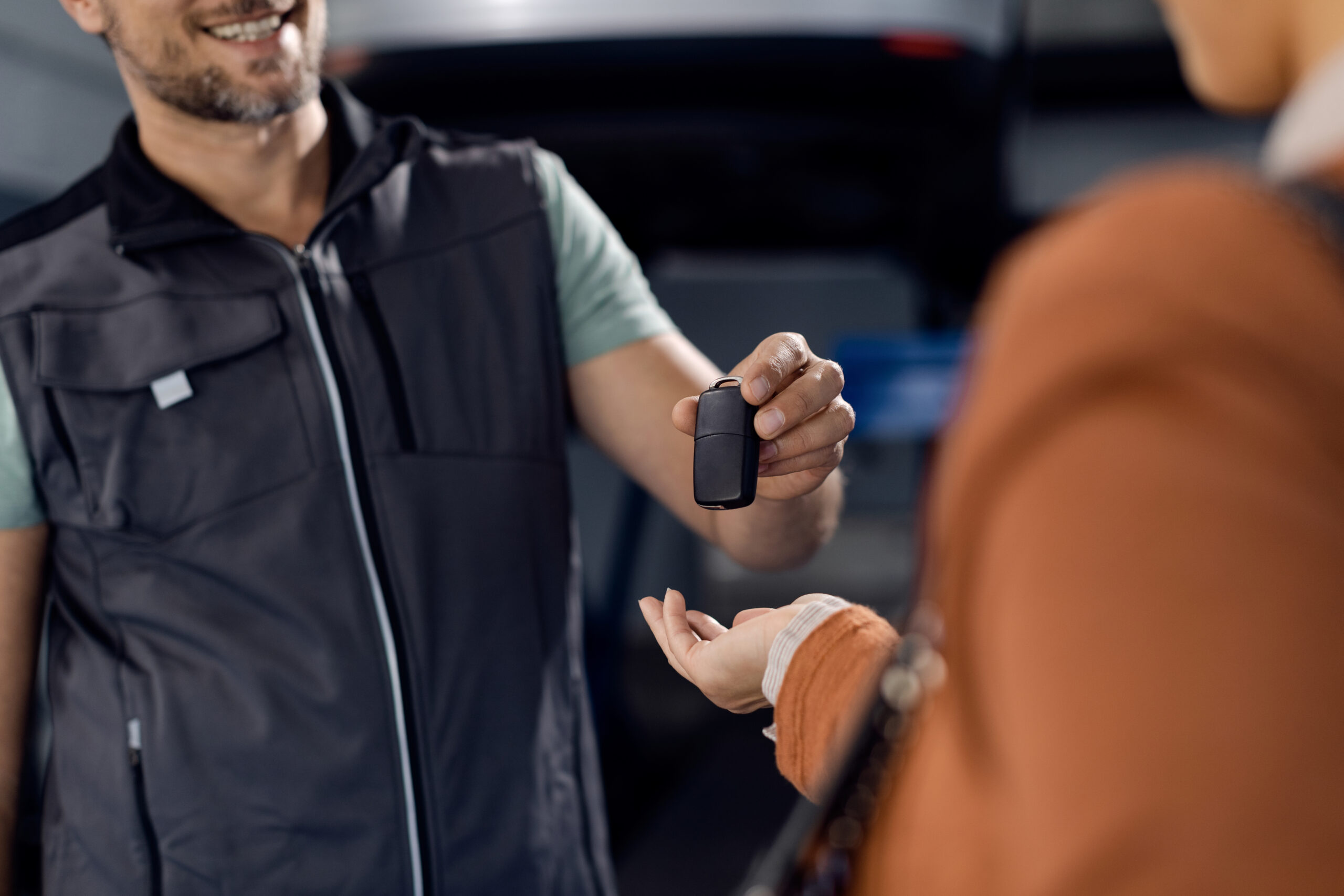 Close-up of mechanic giving car key to a customer at repair shop