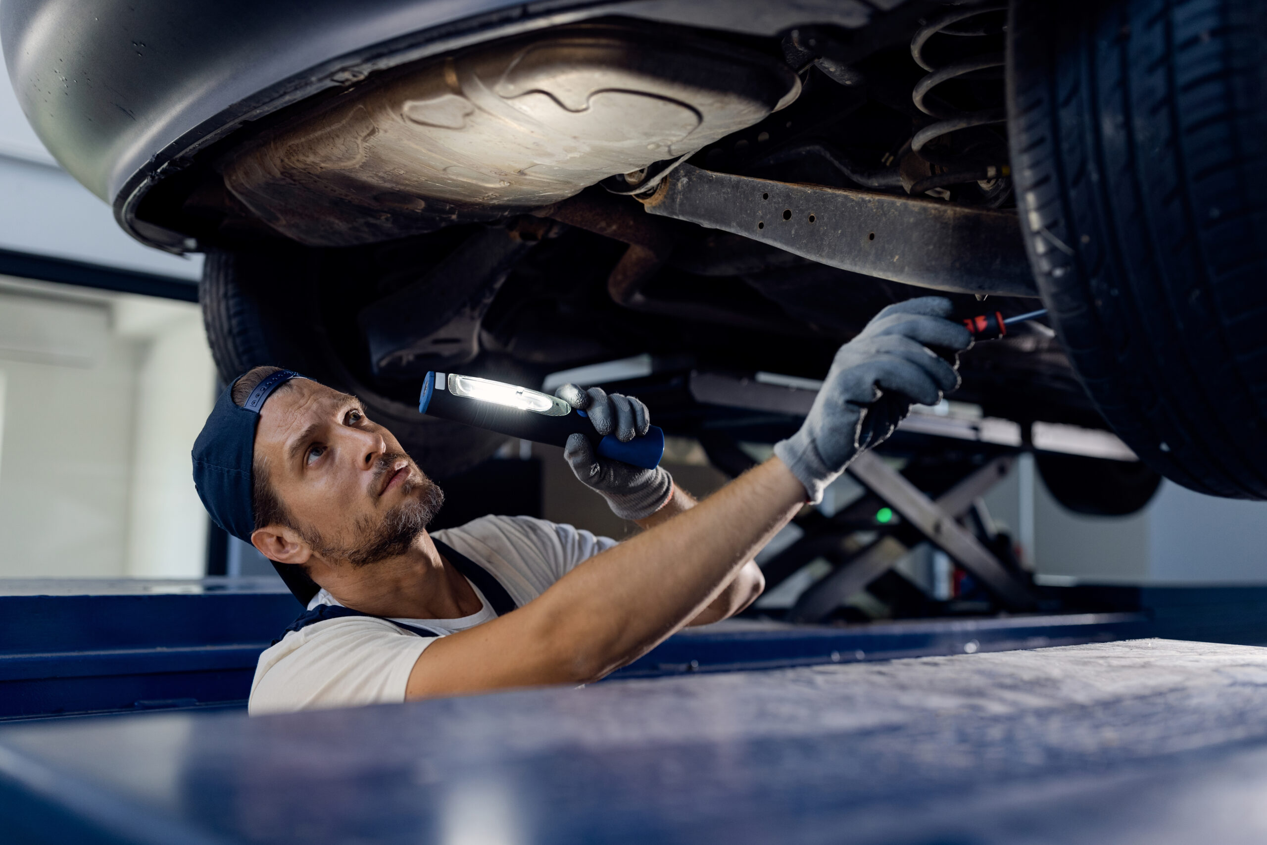 Auto mechanic examining undercarriage of a car with a flashlight