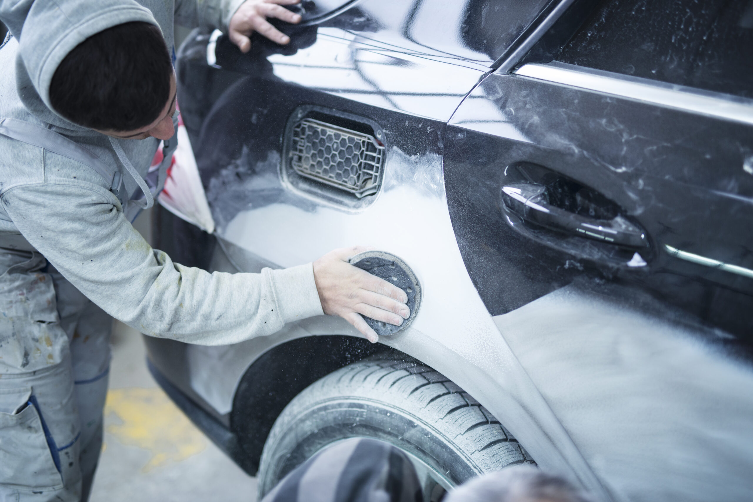 Mechanic worker repairman sanding polishing car body and preparing automobile for painting in workshop garage.