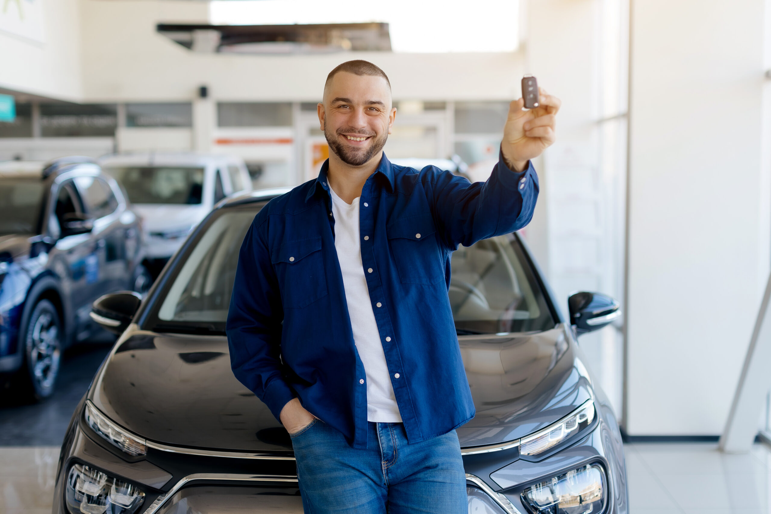 Handsome man customer holding key from auto, buying new car in showroom