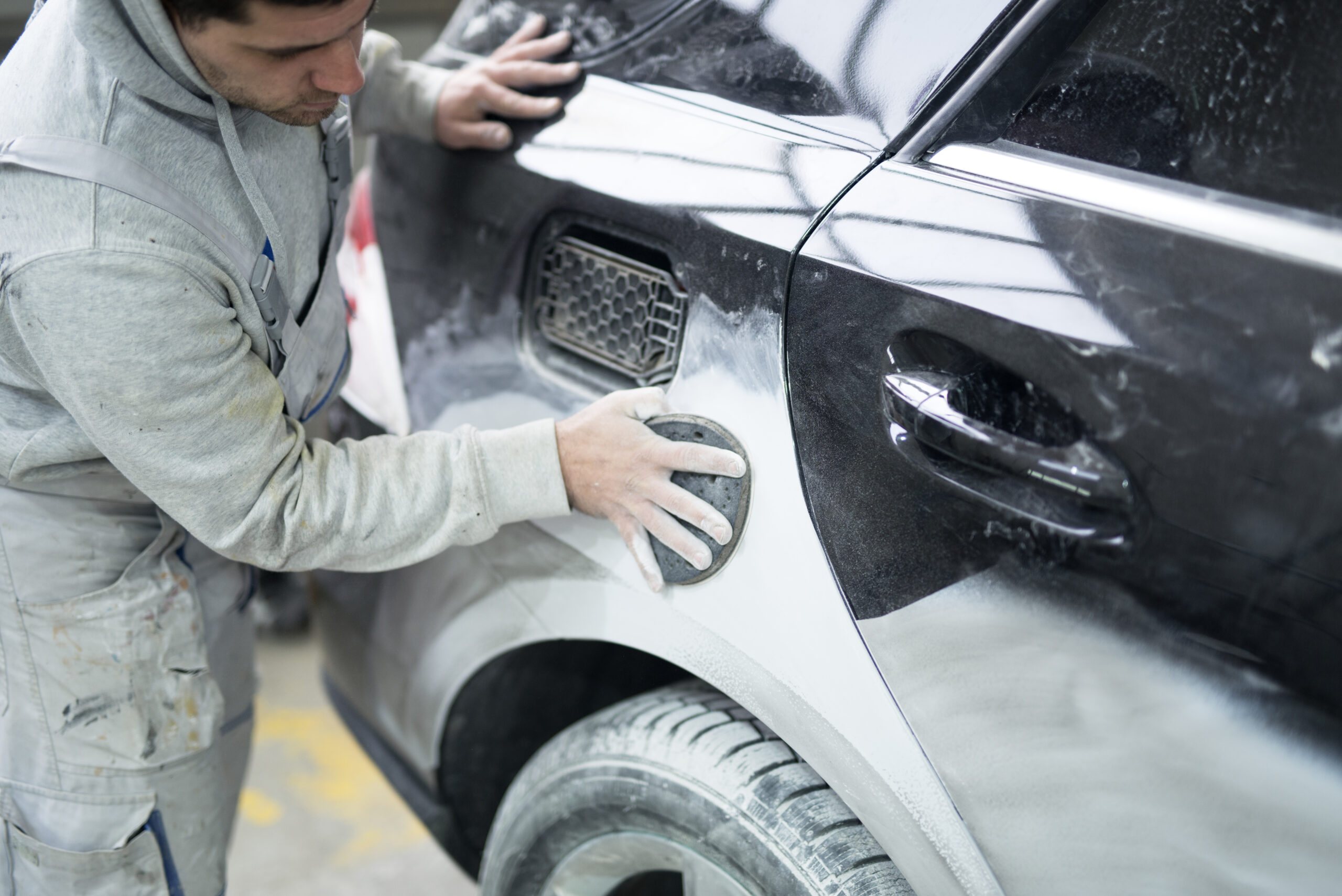 Car painter preparing car for painting in workshop.