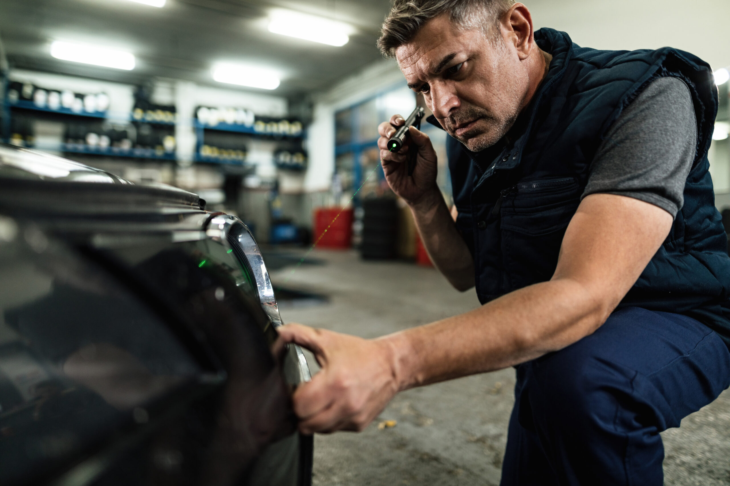 Auto mechanic examining front bumper in repair shop.